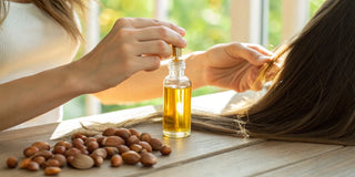 Applying argan oil to hair, with argan nuts and a bottle of oil on a wooden table.